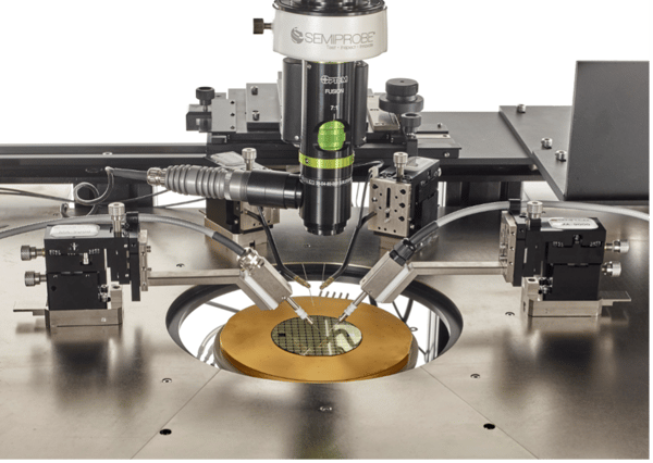 Closeup view of a 3 (75 mm) power transistor wafer affixed via vacuum to a thermal chuck and being probed with manual manipulators up to 3 KV.